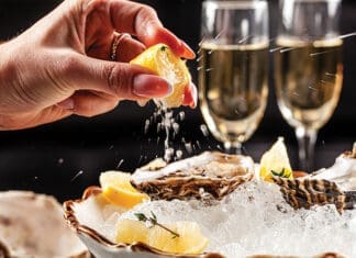 Prosecco Bar Concept. Open Oysters Lie On Crushed Ice With Lemon And Lime, Next To A Glass Of Champagne. Background Image. Copy Space.