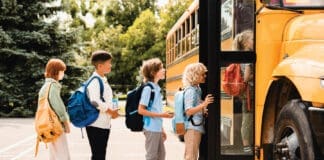 Multiethnic Mixed Race Pupils Classmates Schoolchildren Students Standing In Line Waiting For Boarding School Bus Before Starting New Educational Semester Year After Summer Holidays