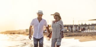 A Middle Aged Couple Walking Hand In Hand On The Beach At Sunset.