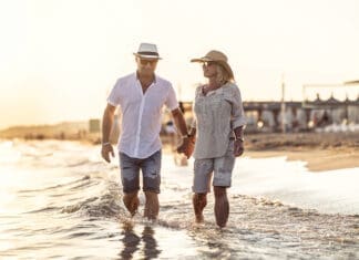 A Middle Aged Couple Walking Hand In Hand On The Beach At Sunset.