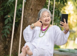 Elderly Woman Relaxing On A Swing While Using A Tablet In A Serene Outdoor Setting