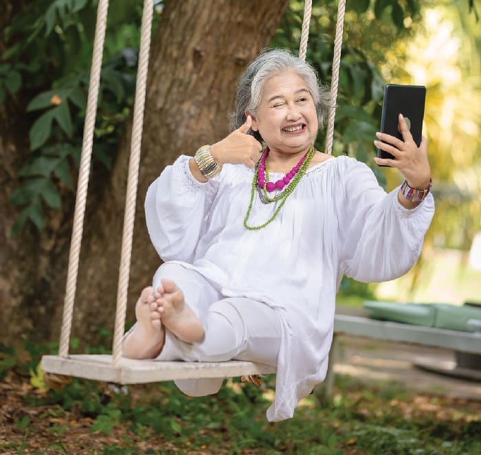 Elderly Woman Relaxing On A Swing While Using A Tablet In A Serene Outdoor Setting